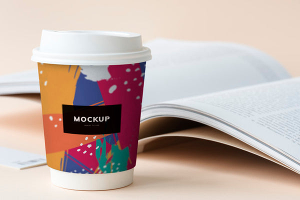 Free Takeaway Coffee Cup Mockup On A Table With An Open Book Psd